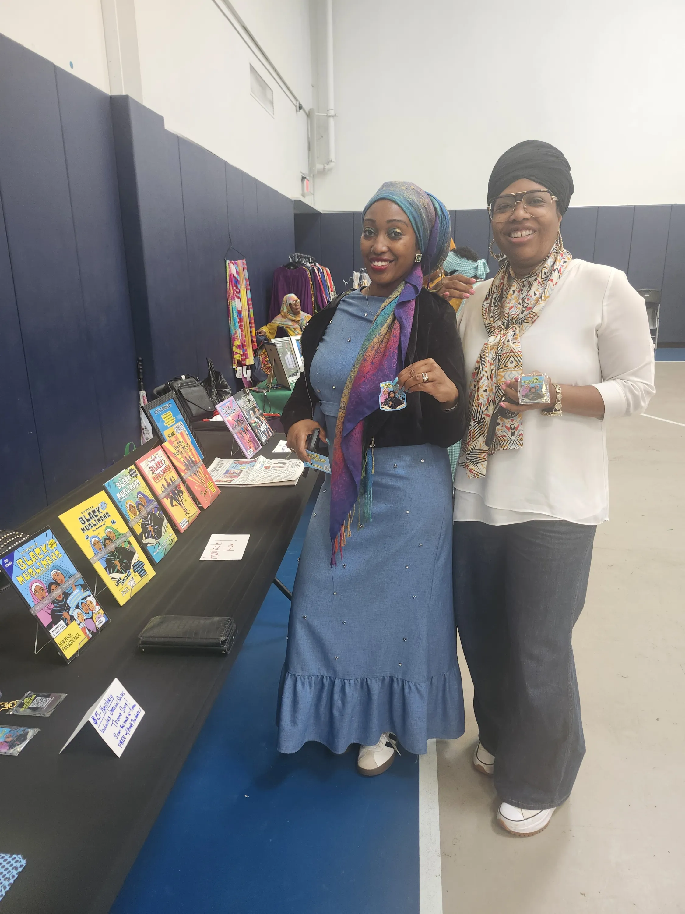Two supporters holding Adventures of Black Muslimahs keychains at a vending event